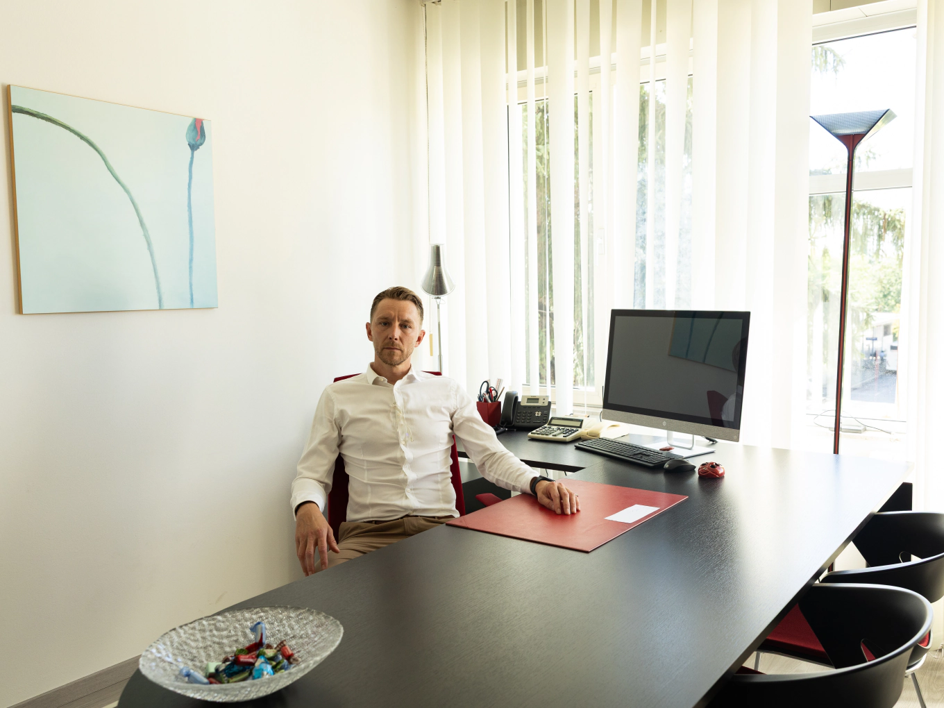 Un consulente seduto alla scrivania di un ufficio luminoso, con il computer e la vetrata alle spalle