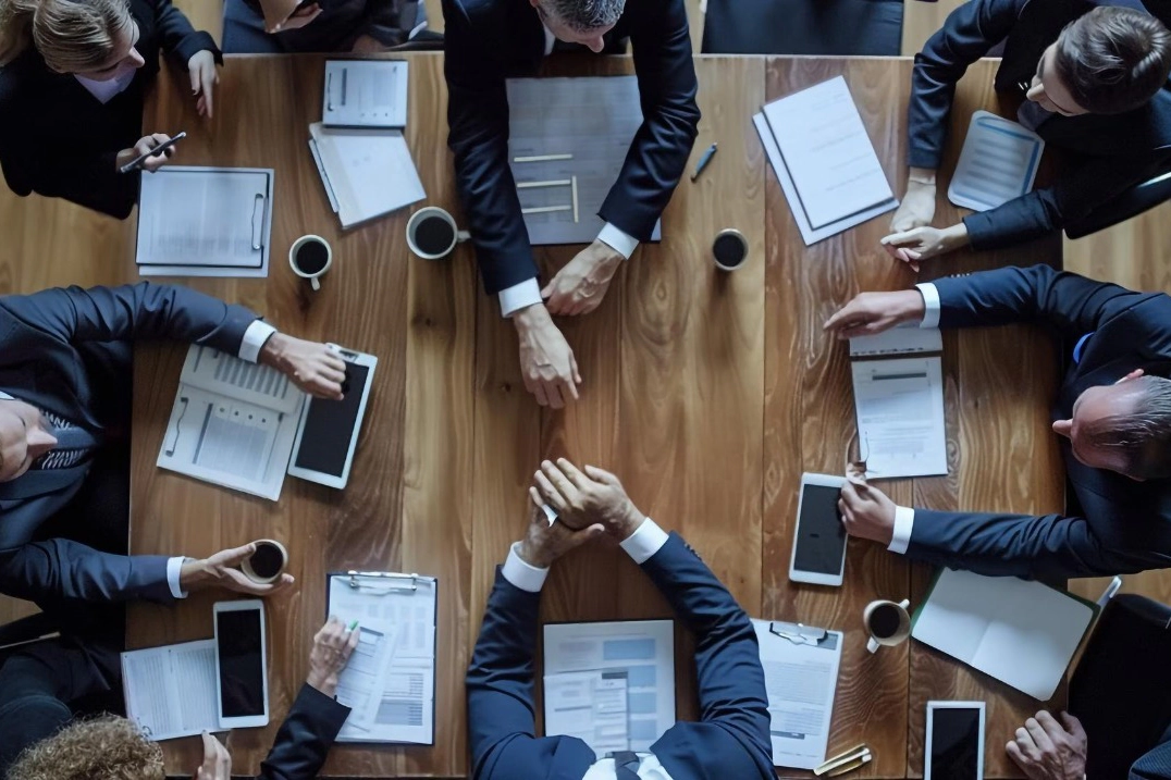 Una riunione di soci vista dall’alto, attorno a un tavolo con documenti e tablet