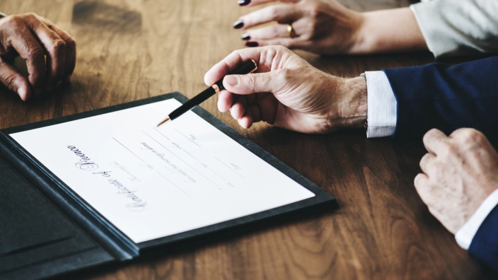 Un professionista indica con la penna il punto della firma su un atto, al tavolo con i soci