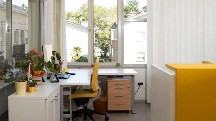 Una postazione di lavoro in un ufficio luminoso, con la scrivania davanti alla finestra e una sedia gialla